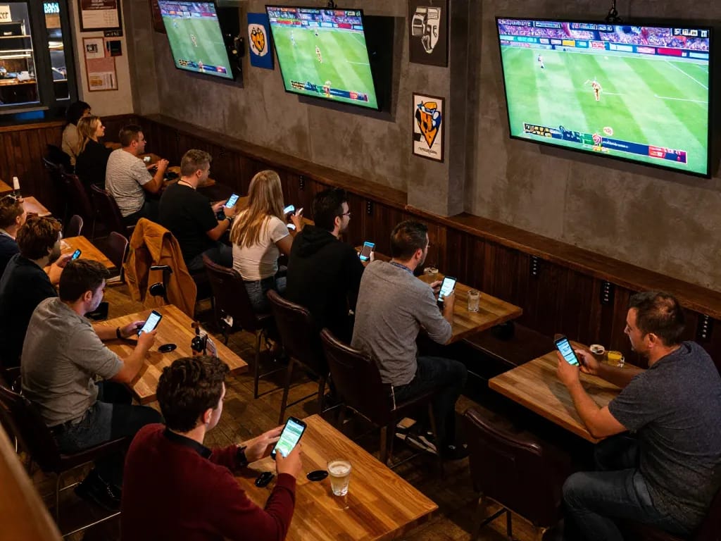 Engaged bettors analyzing odds on their devices at keonhacaii in a lively sports bar atmosphere.